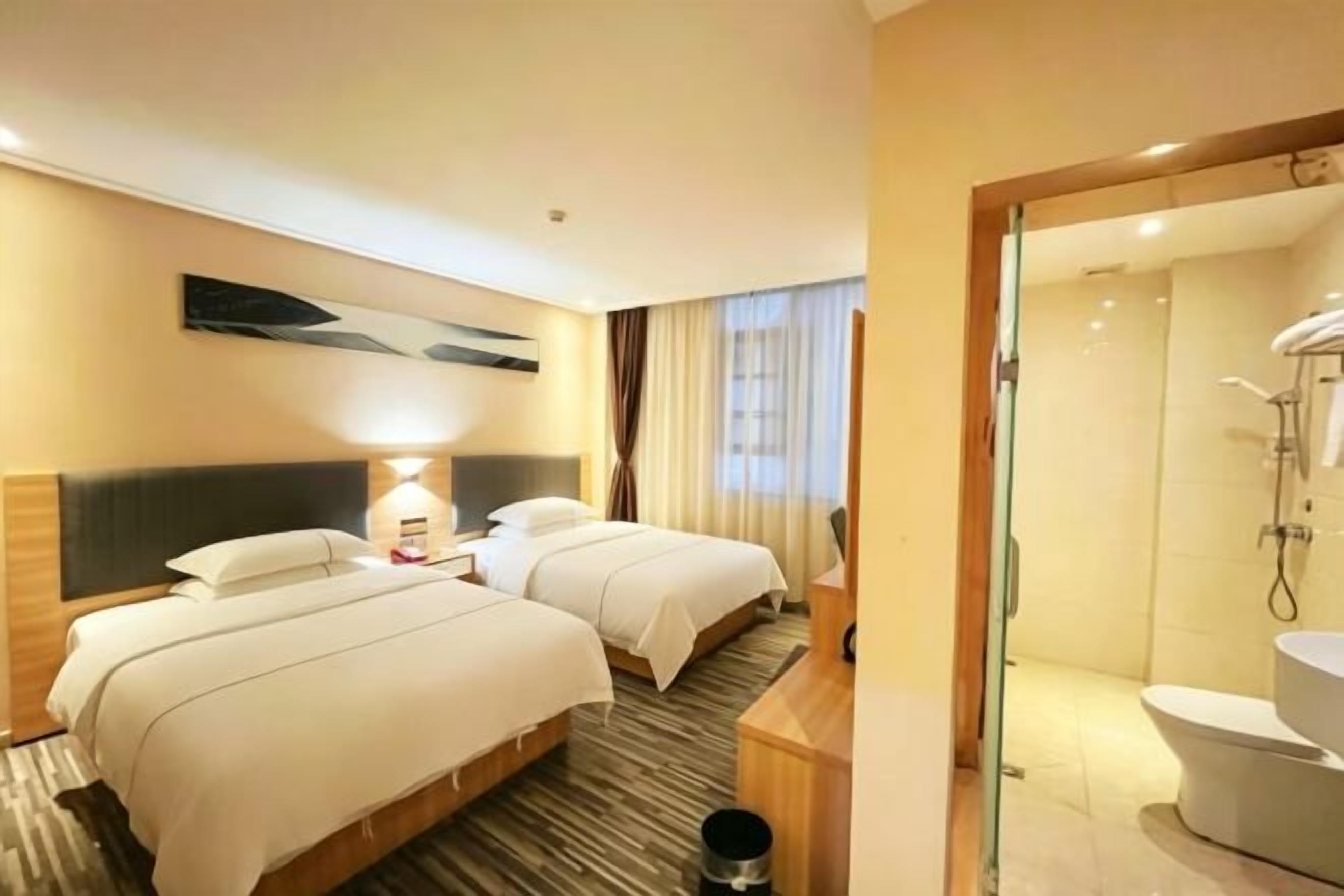 Habitación de hotel con dos camas, un escritorio, una lámpara, zona de ducha y un inodoro.