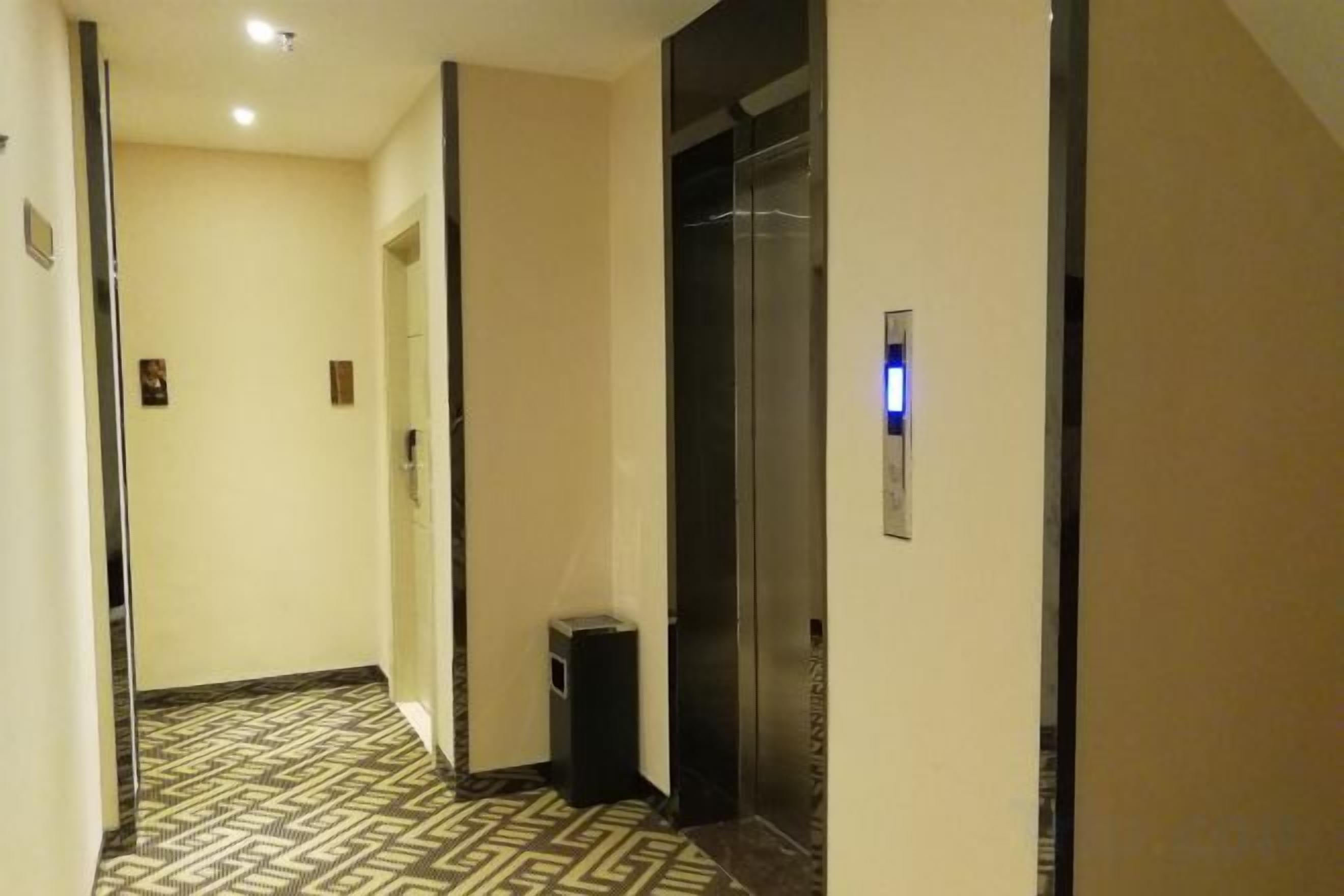 A hotel hallway with a patterned floor, an elevator, and a trash bin.