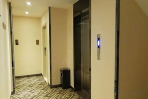 Pasillo de hotel con suelo estampado, un ascensor y un cubo de basura.