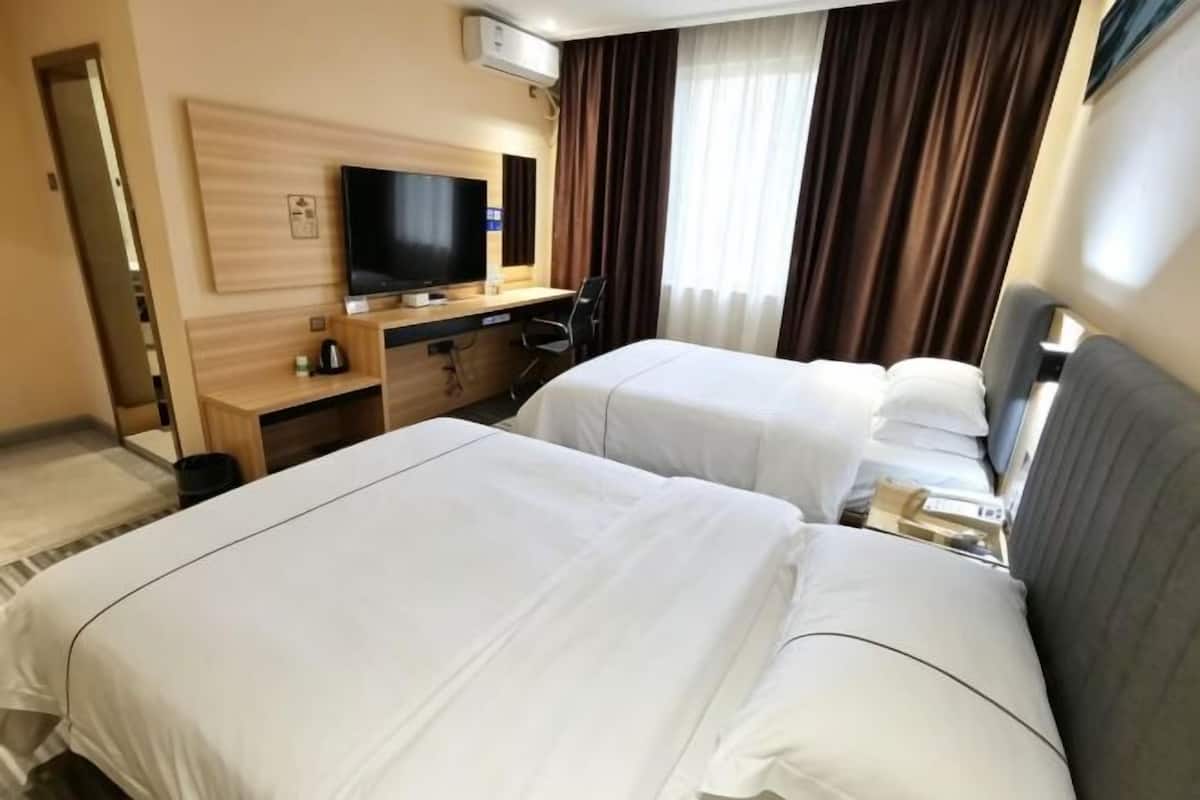 Ein Hotelzimmer mit zwei Betten, einem Fernseher, einem Schreibtisch und einem fenster mit Vorhängen.