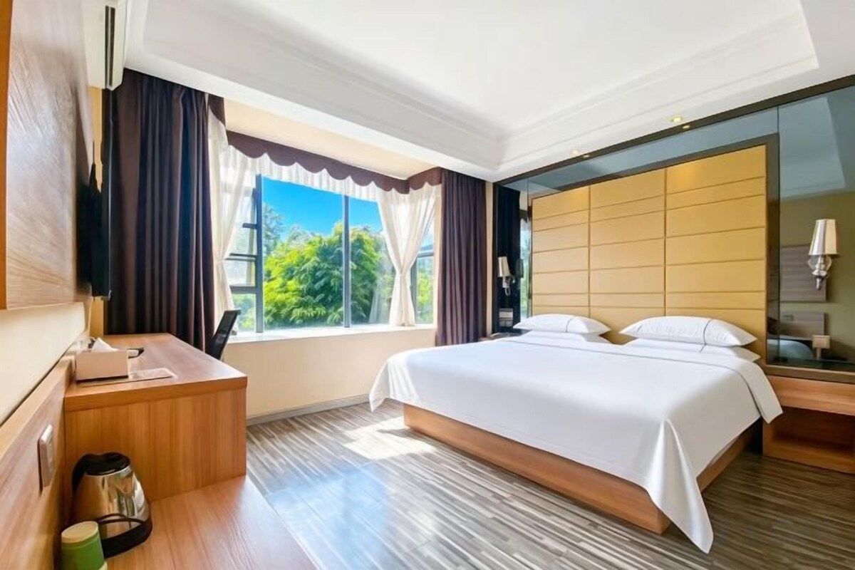 Una habitación de hotel con una cama grande, un escritorio, una silla, un televisor y una ventana con cortinas.