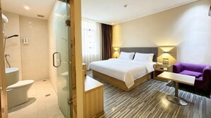 Een hotelkamer met een bed, nachtkastje, stoel en een douchecabine van glas.