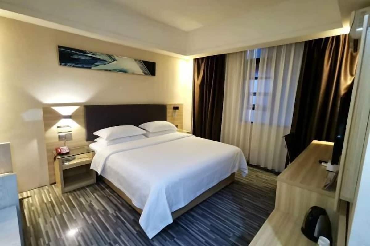 Ein Hotelzimmer mit einem Bett, einem Nachttisch, einer Lampe, einem Bild an der Wand und einem Fenster mit Vorhängen.