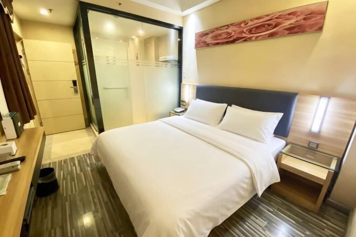 Ein Hotelzimmer mit Bett, Nachttisch, Schreibtisch und Duschbereich.