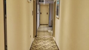 Een gang met een kamerbreed tapijt, beige wanden en deuren die naar kamers leiden.