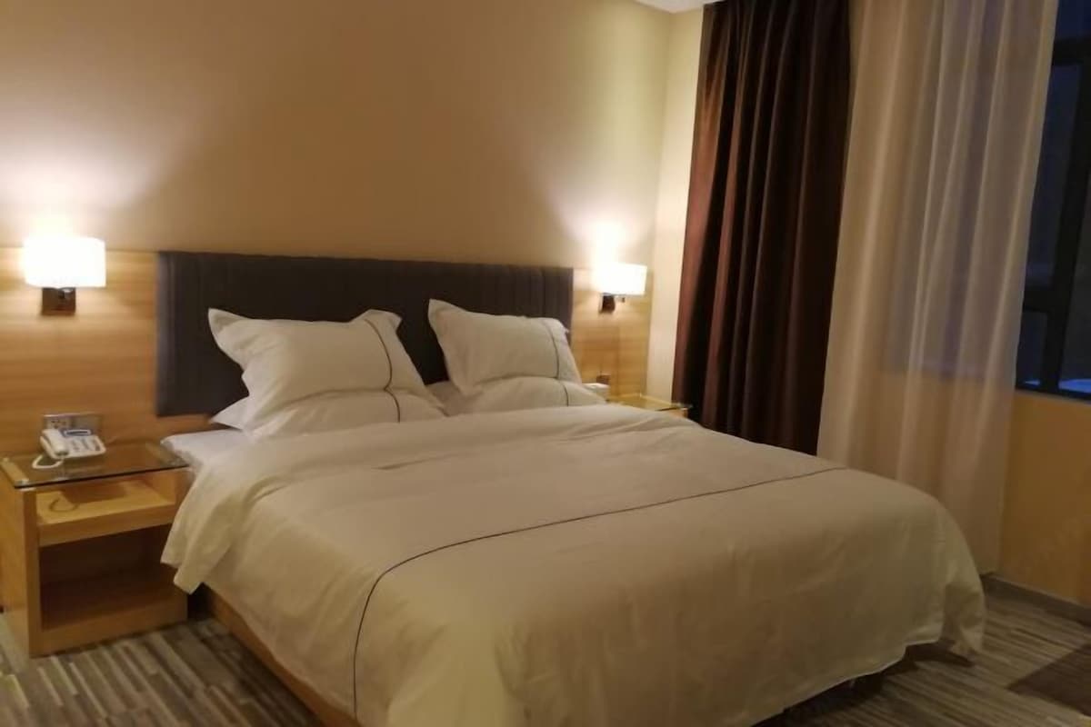 Habitación de hotel con una cama grande, dos lámparas de noche, teléfono en la mesita de noche y una ventana con cortinas.