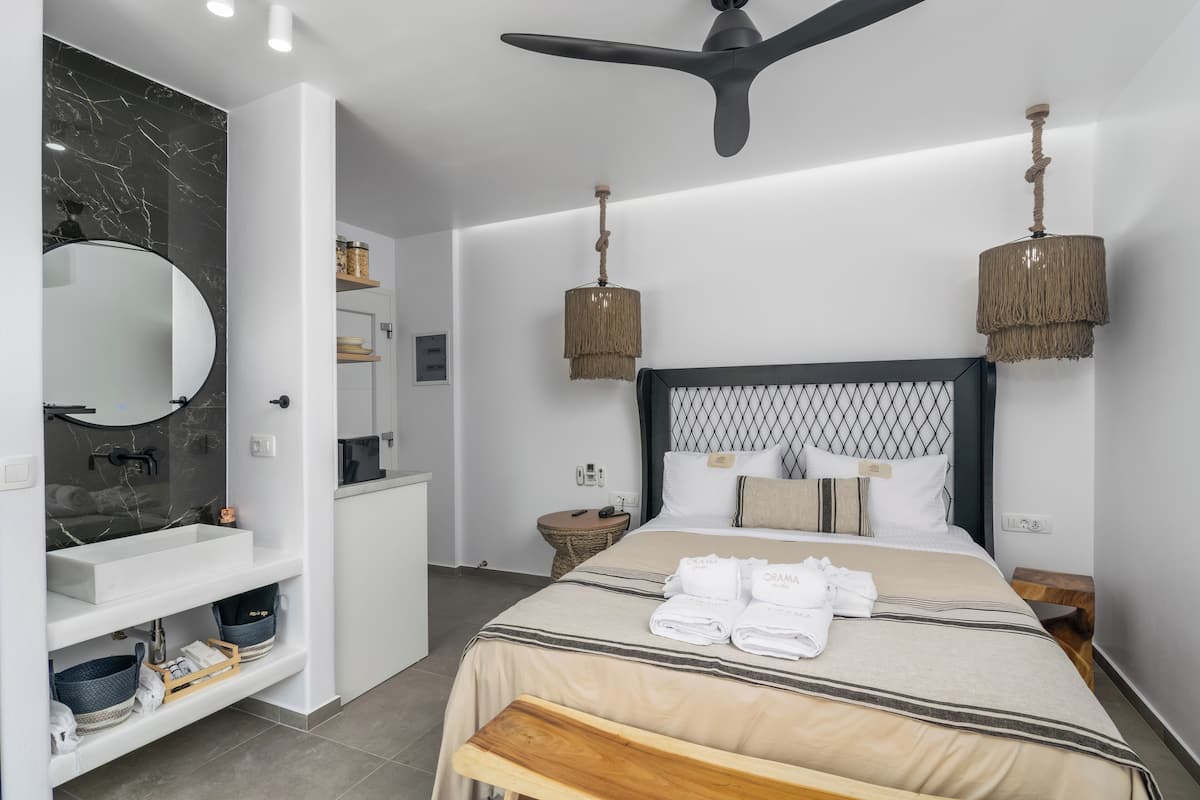 Moderni hotellihuone, jossa on suuri sänky, pyöreä peili, puinen penkki ja kattotuuletin.