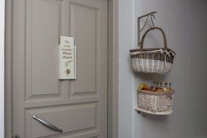 A door with a sign instructing to clean the room, a basket hanging on a hook, and a basket shelf with food items. - Orama Milos (Milos)