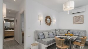 A modern living room with a grey sectional sofa, a dining table with four chairs, and a chandelier. - Orama Milos (Milos)