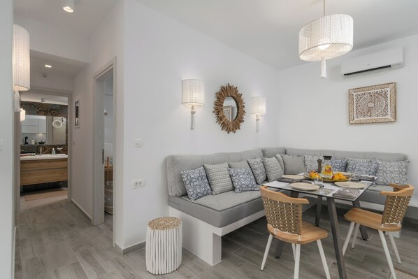 A modern living room with a grey sectional sofa, a dining table with four chairs, and a chandelier. - Orama Milos (Milos)