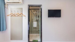A hotel room with a glass shower enclosure, a mounted TV, and a wall-mounted air conditioning unit. - 7 Days Premium Hotel (Guangzhou International Finance City Tangdong Metro Station) (Guangzhou)