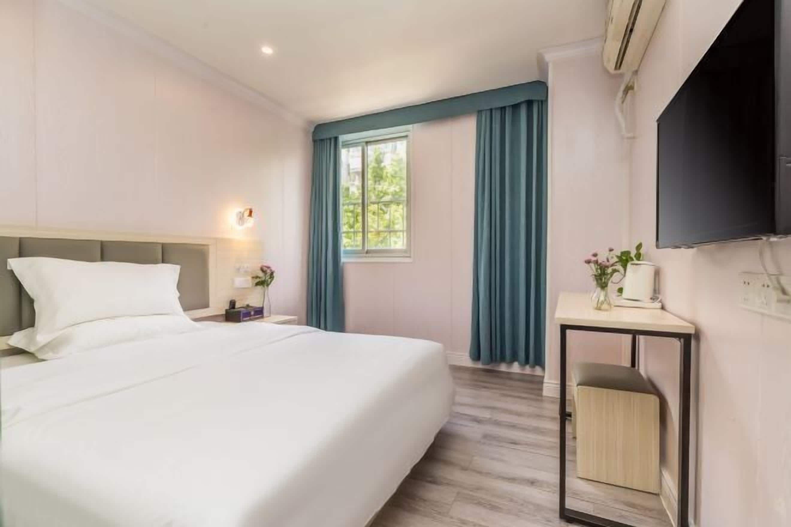 A hotel room with a bed, a desk, a chair, a TV, and a window with curtains.