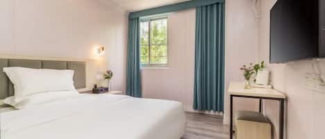 A hotel room with a bed, a desk, a chair, a TV, and a window with curtains.