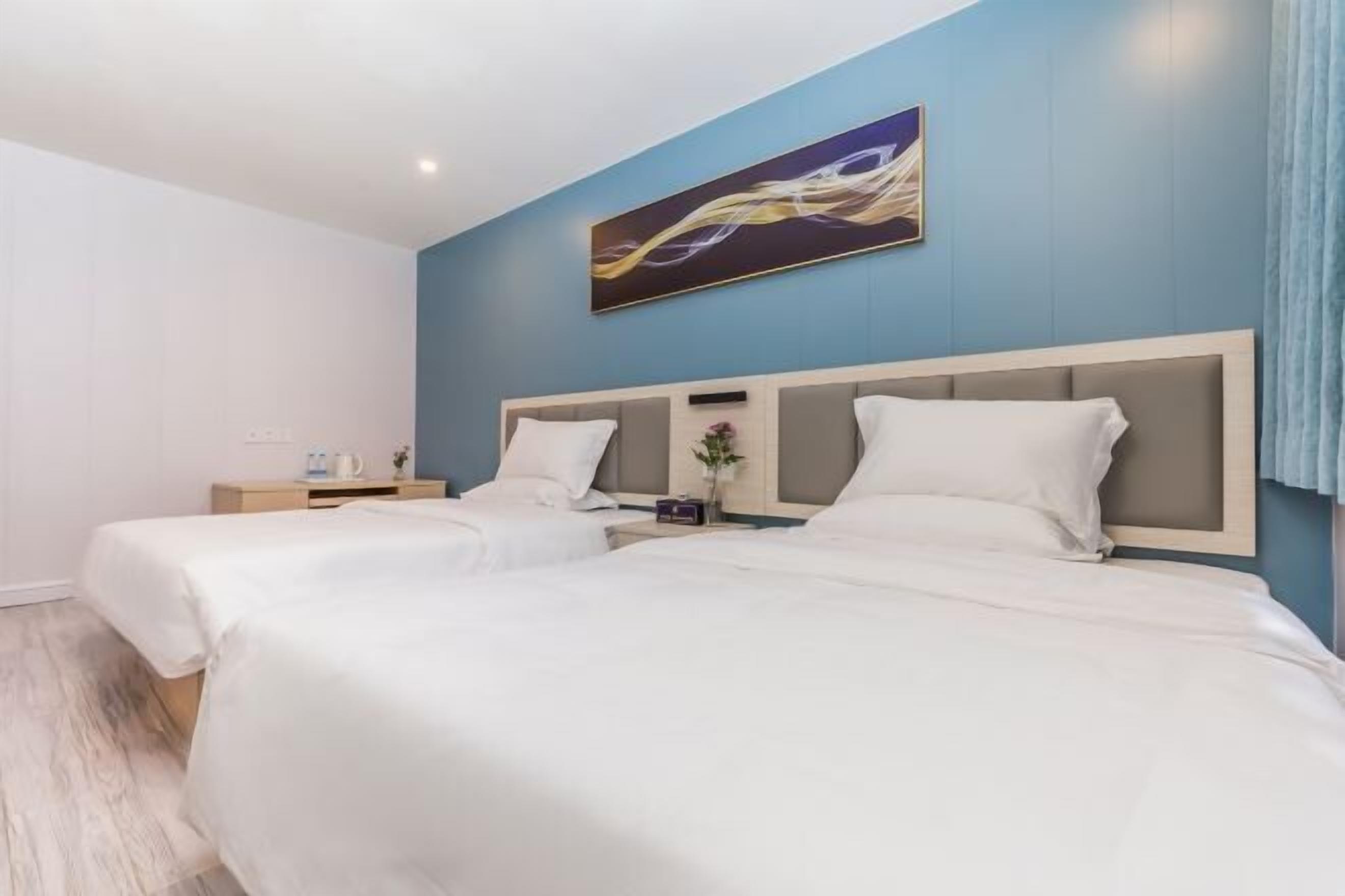 A hotel room with two beds, a blue accent wall, and a painting above the beds.