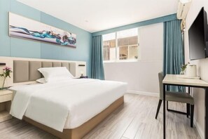 Habitación de hotel con cama, escritorio, silla, televisor y ventana con cortinas.