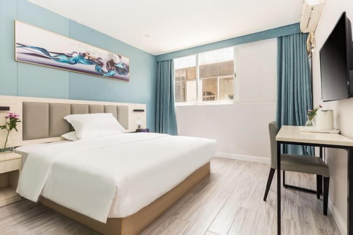 A hotel room with a bed, a desk, a chair, a TV, and a window with curtains.