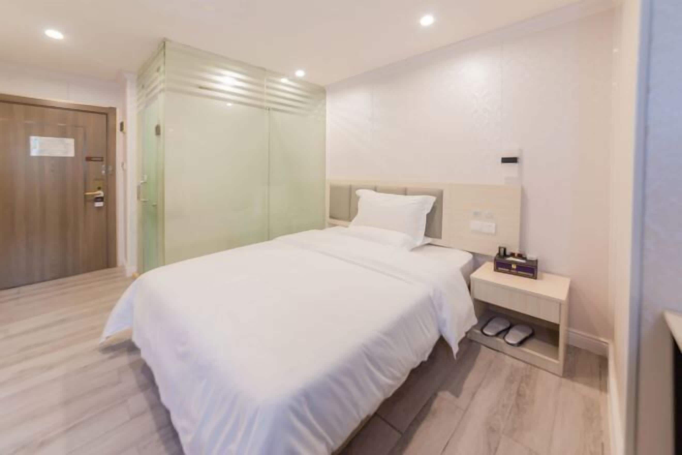 A bedroom with a bed, a nightstand, a shoe rack, and a door.