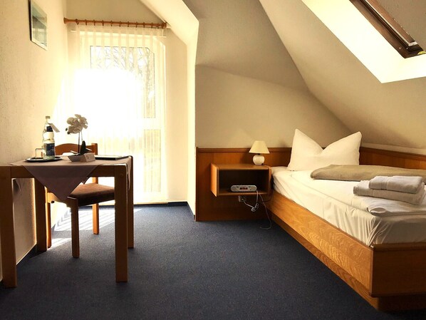 A hotel room with a bed, bedside table, lamp, and a small table with a chair. - Hotel Nordwind Lohme (Lohme)