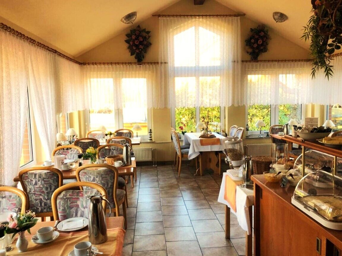 Un comedor con varias mesas y sillas, una barra de buffet con exhibición de alimentos y amplias ventanas que dejan entrar luz natural.