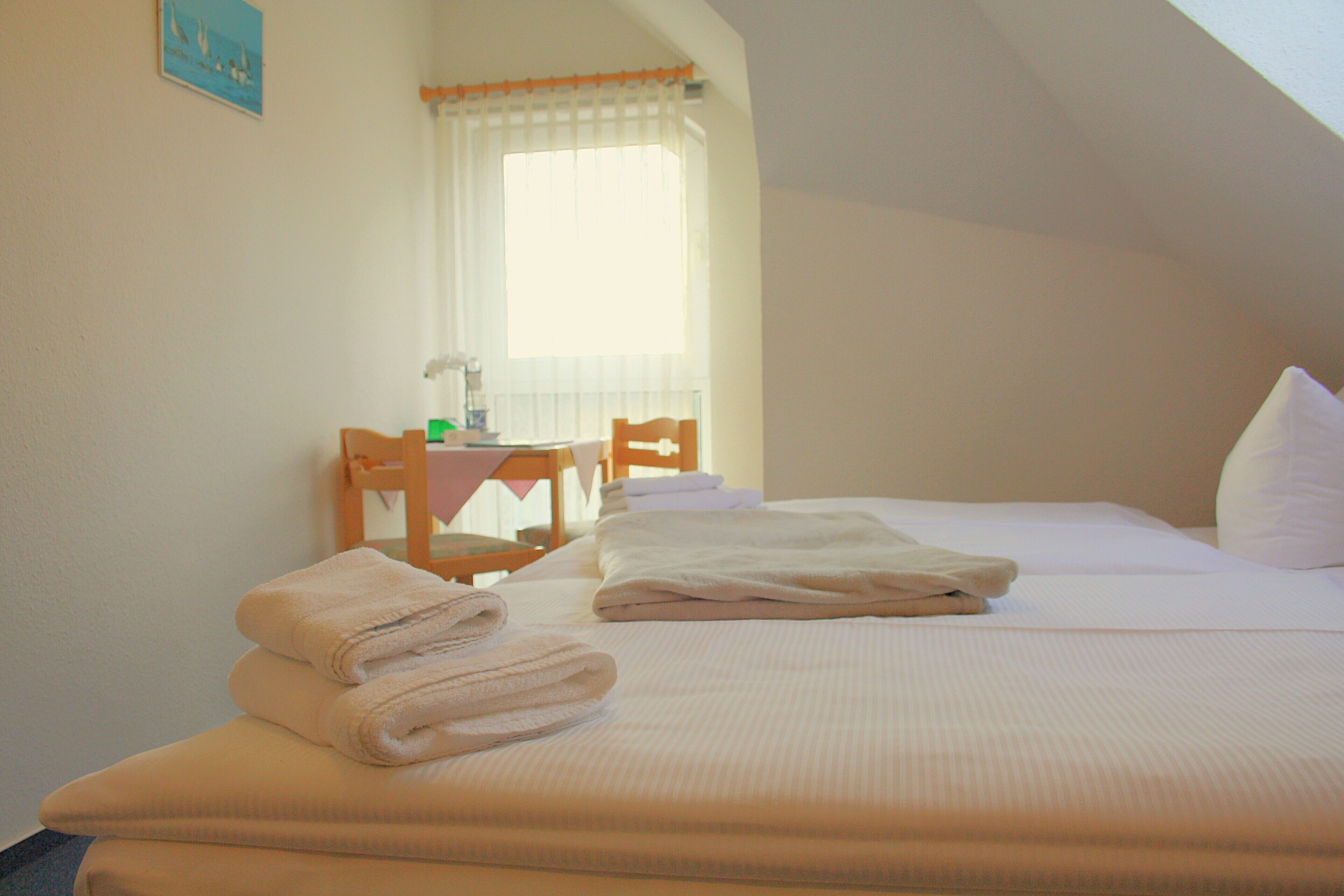 A neatly made bed with folded towels, a wooden chair, and a small table with a lamp.