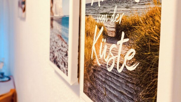 Two framed pictures on a wall, one depicting a beach scene and the other featuring text in a foreign language. - Hotel Nordwind Lohme (Lohme)
