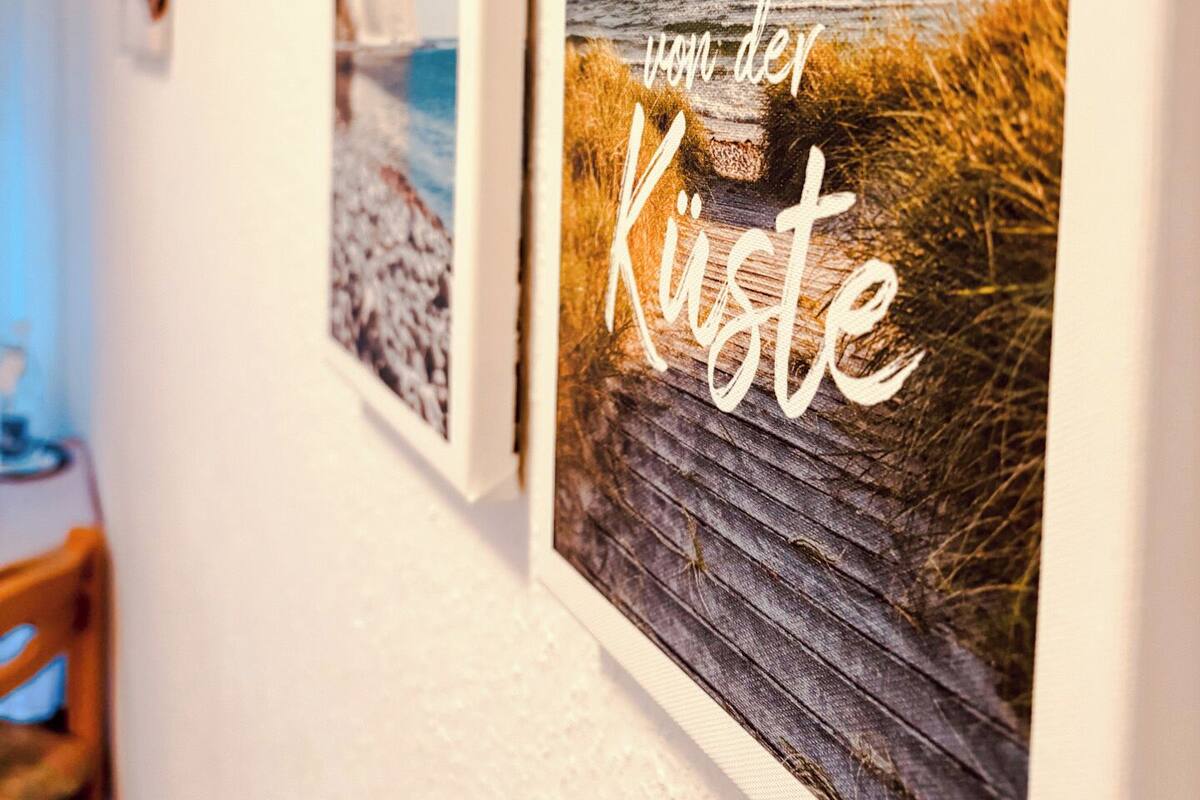 Dos cuadros en una pared, uno con una playa y el otro con texto en un idioma extranjero.