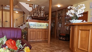 A reception area with a wooden desk, a ship model, a staircase, and a purple sofa. - Hotel Nordwind Lohme (Lohme)