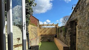 En terrasse med et træpergola, stenvægge og et lille haveområde.
