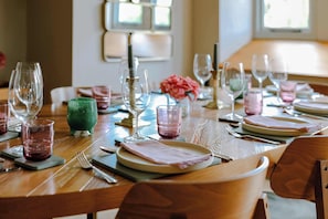 A dining table set with plates, glasses, and cutlery, with a vase of flowers and a candle on the table. - Iron Mill House - Riverside Hot Tub - Frome (Somerset)