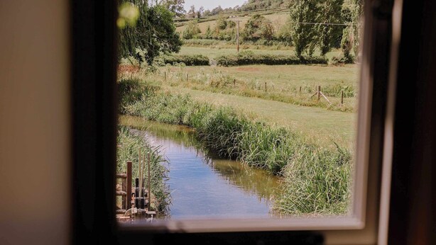 Blick aus dem Fenster auf einen Fluss, umgeben von Grün und einer Holzzahlung.