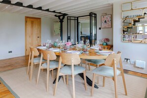 Comedor con una mesa redonda dispuesta para seis personas, rodeada por seis sillas con cojines de colores claros.