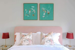 A bed with a pink headboard, two pillows with floral designs, and two red lamps on either side. - Iron Mill House - Riverside Hot Tub - Frome (Somerset)