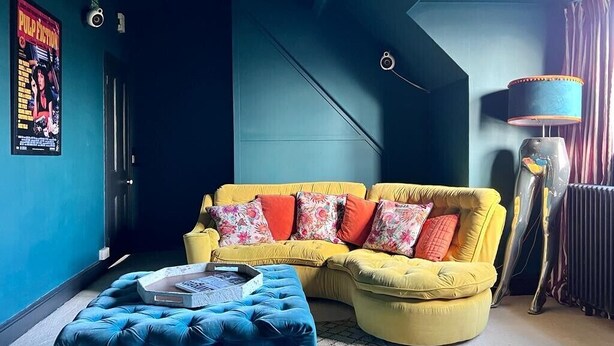 A room with a yellow sofa, a blue ottoman, a lamp, and a poster on the wall. - Edwardian Town House - Garden & Cinema (Somerset)