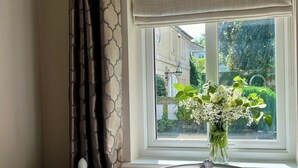 A bedroom with a window, a bed, and a vase of flowers on the windowsill. - Leaze Garden Cottage - Frome (Somerset)