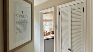 A hallway with a framed sign, a door, and a glimpse of a kitchen area. - Leaze Garden Cottage - Frome (Somerset)