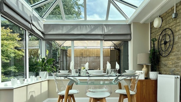 A conservatory with a glass table and chairs, a stone wall, and a view of greenery. - Leaze Garden Cottage - Frome (Somerset)