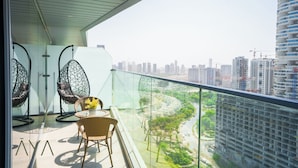 Ein Balkon mit Korbstühlen und einem Tisch, Blick auf eine Stadtlandschaft mit Hochhäusern und Baukränen.