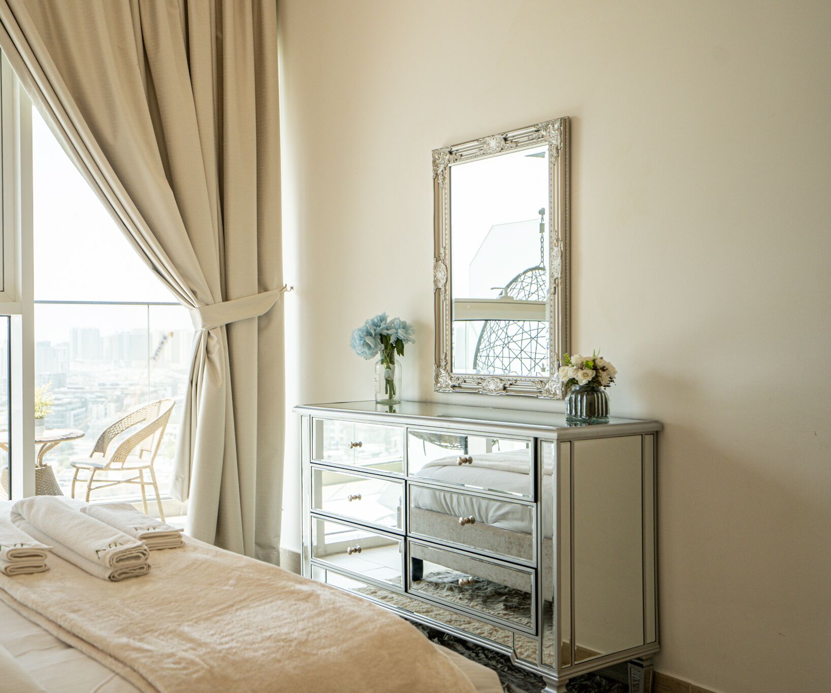 Une chambre d’hôtel avec un lit, une coiffeuse avec un grand miroir et une vue sur la ville grâce à de larges fenêtres.