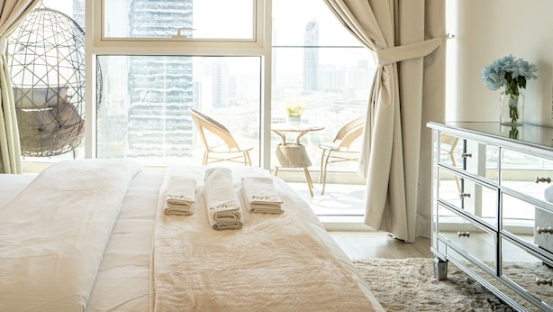 Ein Hotelzimmer mit einem großen Bett, Blick auf die Stadt, einer Essecke mit Stühlen und einem Dekorsessel.