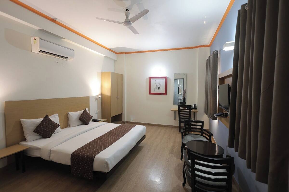A hotel room with a bed, a desk, a chair, a ceiling fan, and a TV.