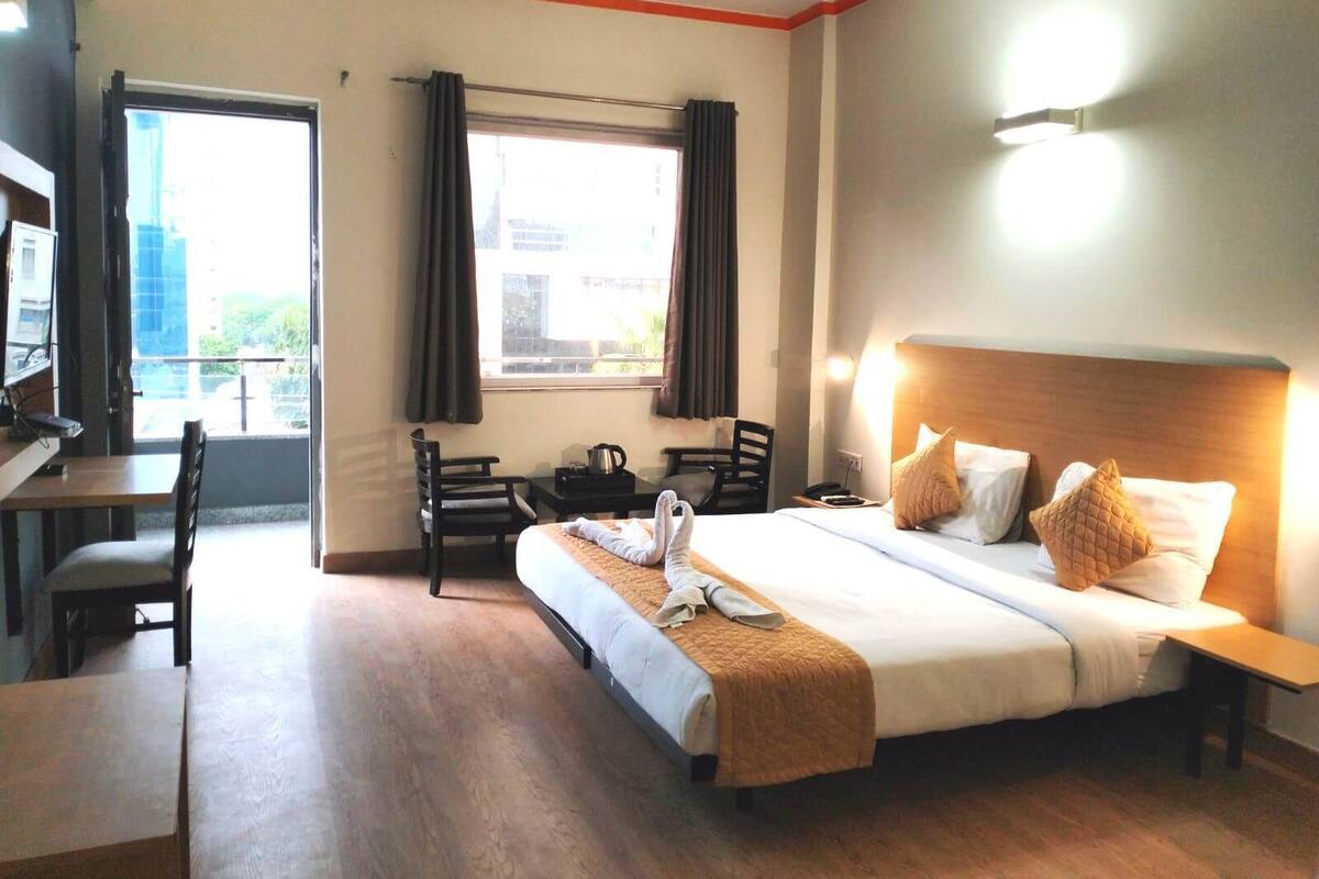 A hotel room with a bed, bedside table, chair, desk, and a window with curtains.