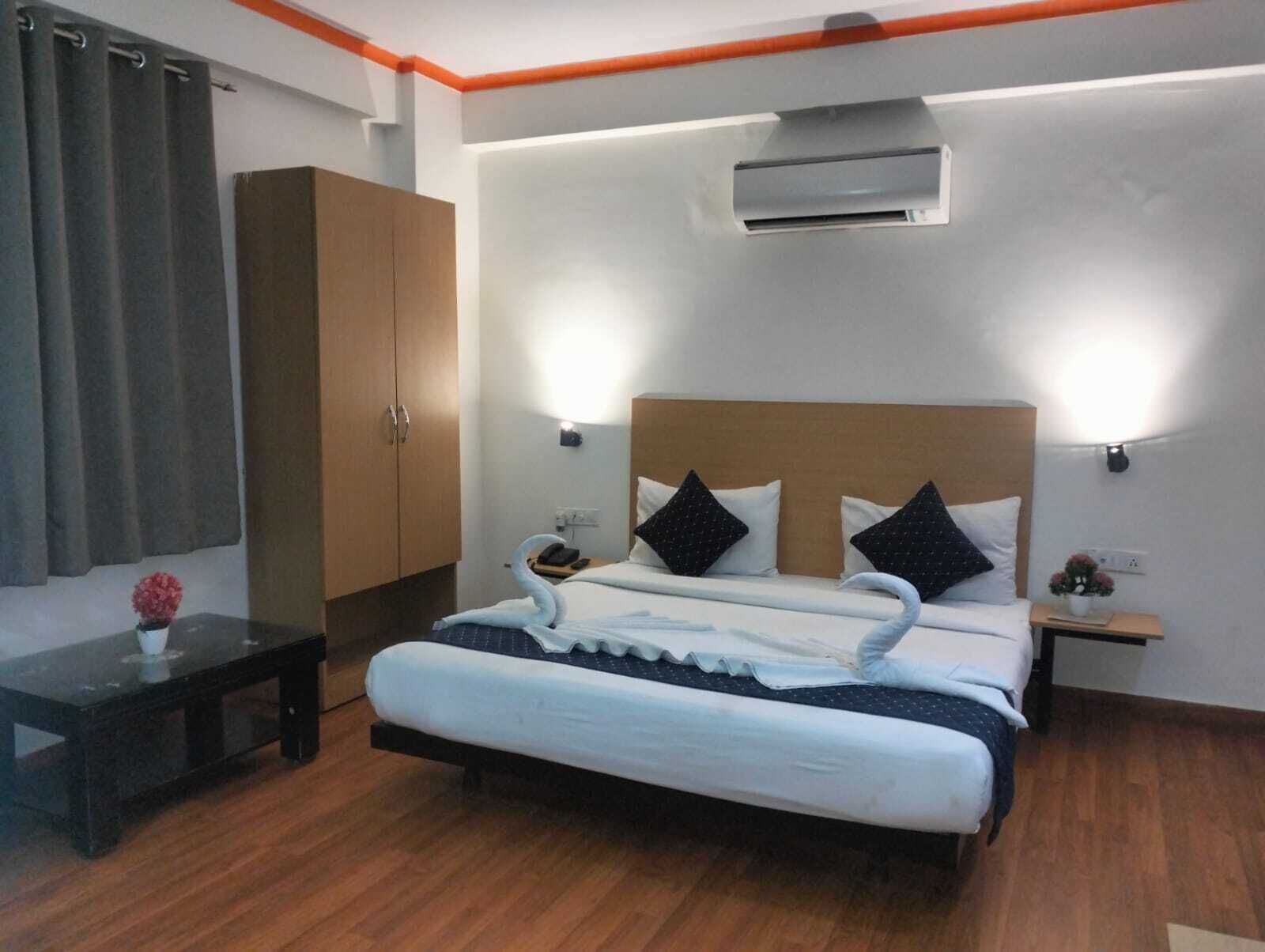 A modern hotel room with a large bed, wooden wardrobe, bedside tables, and an air conditioning unit.