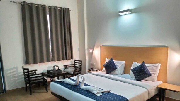A hotel room with a bed, a desk, a chair, and a window with curtains. - hotel noida express (Noida)