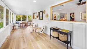 Ein geräumiges Zimmer mit Holzboden, einem Essbereich mit Stühlen und Tisch, einem großen Spiegel und einem Deckenventilator.