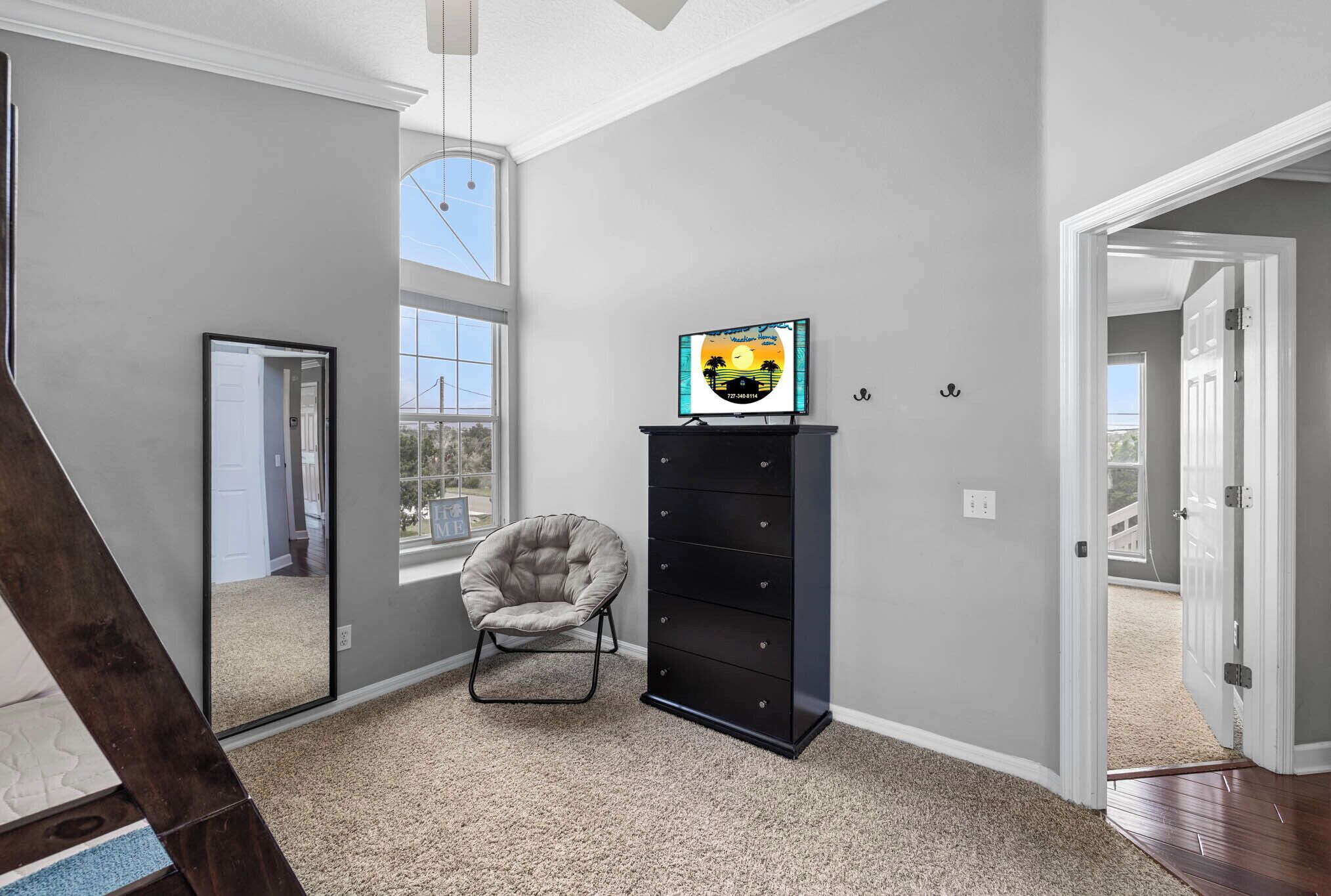 A room with a large window, a chair, a black storage unit, and a door leading to another room.