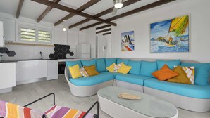 A modern living room with a sectional sofa, a glass coffee table, and a dining area with a kitchen in the background.