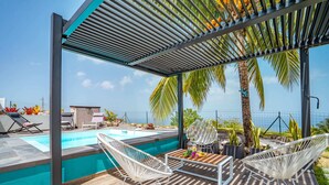 A modern outdoor pool area with a pergola, lounge chairs, and a view of the ocean.