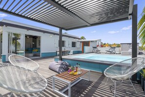 Un espacio al aire libre cubierto con piscina, sillones de descanso y una mesa con bebidas.