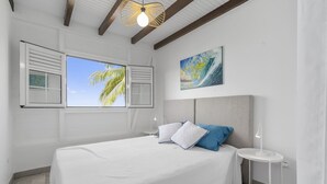 A bedroom with a bed, a nightstand, a painting, and a window with shutters.