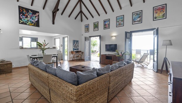 Un salón amplio con un sofá tejido, un comedor con mesa y sillas, un televisor y un balcón con una silla.